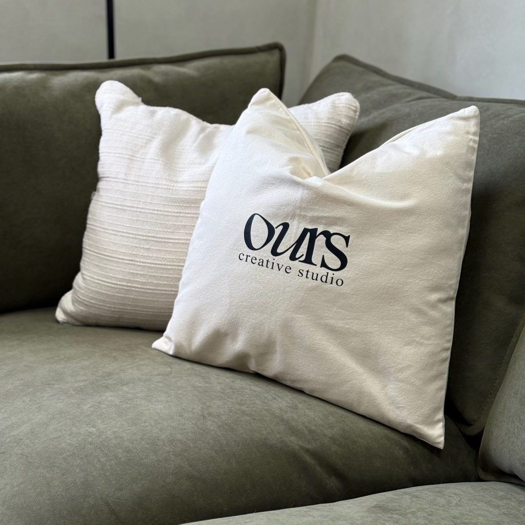 Decorative cushions with the logo of Ours Creative Studio on a green sofa.