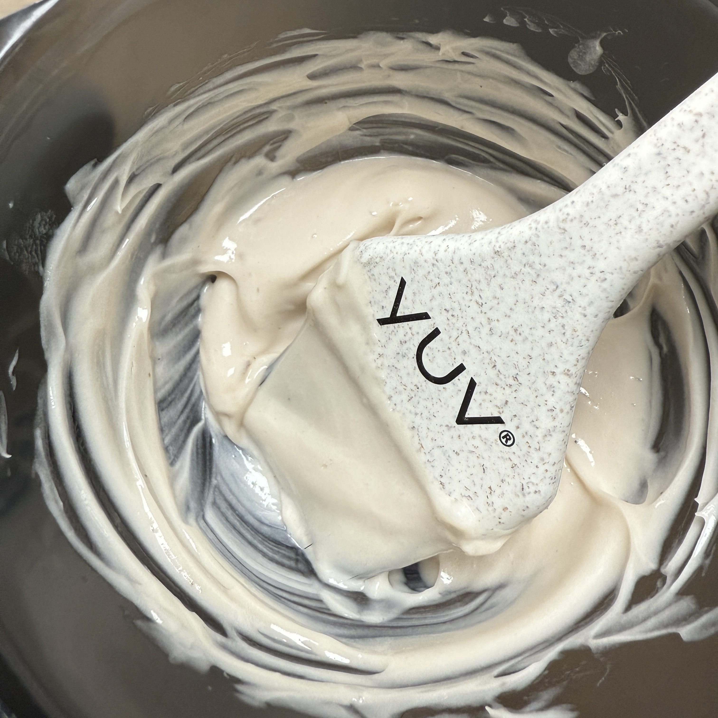 A close-up of a mixing bowl containing a creamy hair dye mixture, with a spatula bearing the YUV® logo resting inside.