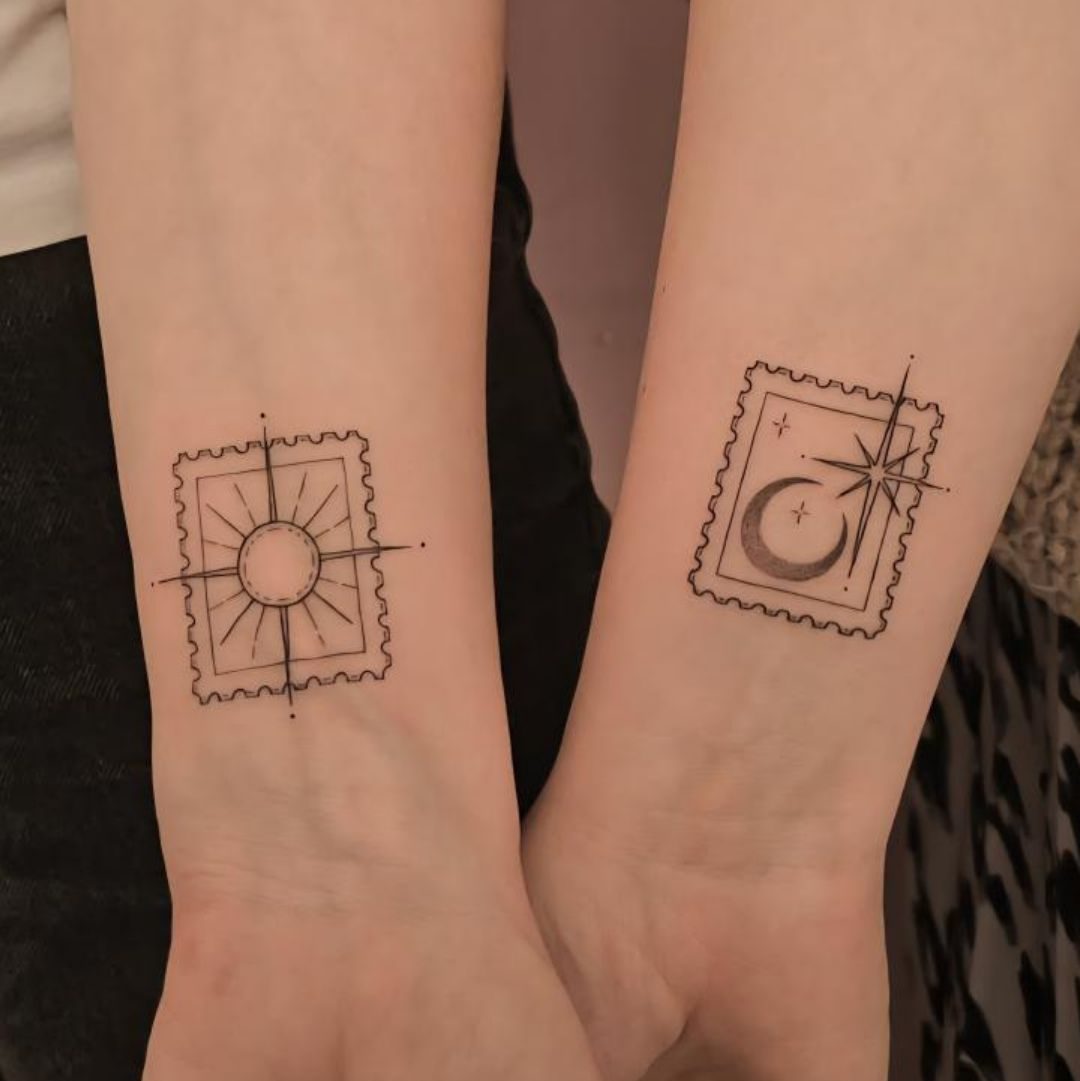 A close-up of two arms displaying matching fine-line tattoos of a sun and a moon inside stamp-like outlines.